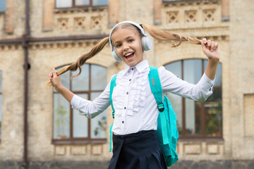 Happy school girl in uniform having fun listening to music in headphones and holding hair