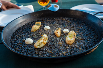 Black rice with cuttlefish and young garlic, a dry rice dish, cooked in paella or in a clay pot, a characteristic flavor of Valencian Mediterranean cuisine. Spain