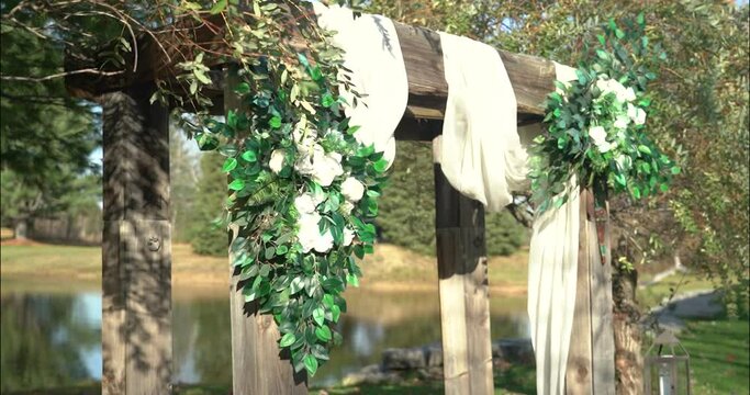 Beautiful wedding arbor with white draping cloth, white rose bouquets with a pond and woods in the background in Ottawa, Ontario (Bean Town Ranch). 