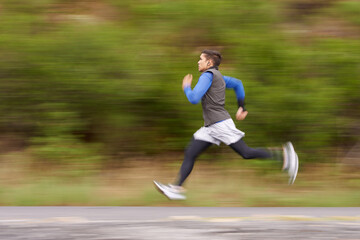 Burning away the miles. Motion blurred image of a young man running along the road.