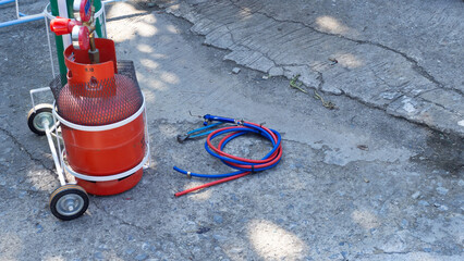 An orange gas cylinder and a hose for welding steel are placed on the ground.