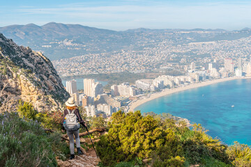 A young hiker descending from the top of the Penon de Ifach Natural Park with the city of Calpe in...