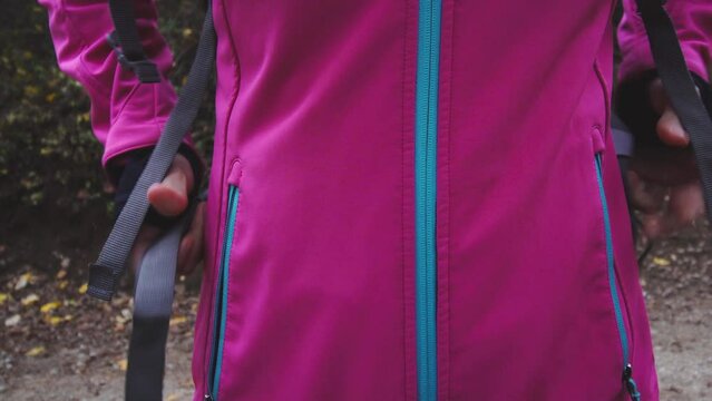 Hiking girl with pink jacket moving zipper on a dirtroad or trail in mountain forest. Travel and healthy lifestyle outdoors in fall season. Front view..