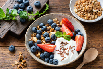 Granola with greek yogurt and berries strawberry blueberry in bowl topped with flax seeds. Rustic wooden table background. Clean eating, dieting concept
