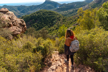Naklejka premium A young hiker girl descending from the top of the El Garbi mountain, the spectacular viewpoint of the Sierra Calderona, Valencia, a 593-meter mountain. Mediterranean Sea. Spain