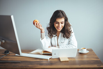 Diet while lockdown. Pretty lady dietologist holding apple in her hand and smiling, recommending fresh fruits, posing at clinic, copy space. Online consultation