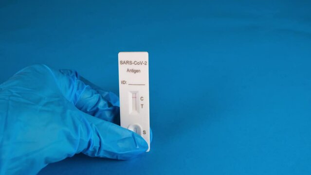 hand in a protective medical glove holds a Negative SARS-CoV-2 Rapid Antigen Test on a blue background