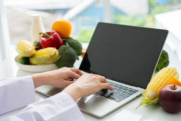 Portrait of Asian smiling female nutritionist typing on laptop computer for balanced corrective...