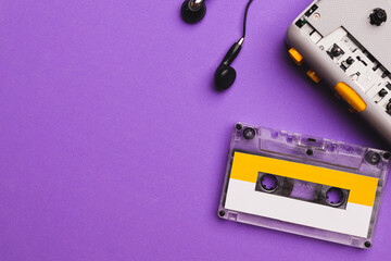 Cassette player with earphones and cassette tape on purple background. Copy space for text.