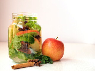 Detox water with apple, cinnamon, star anise and mint. Glass jar with drink, whole apple and cinnamon sticks. On a white background
