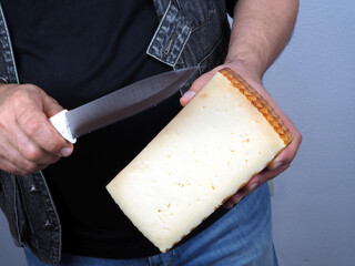 A man holds in his hands half a large head of aged cheese and a knife. The concept of natural farm products
