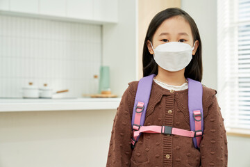 Elementary school Korean girl wearing a mask with a backpack in front of the kitchen