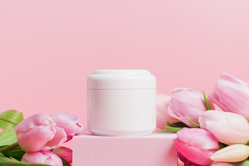 Mockup unbranded white bottle of cream on podium with tulips flowers, spring body and face skin care