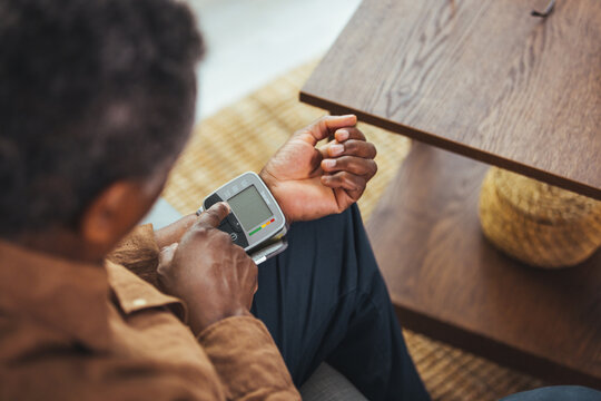 Hypertension In Older Age. Senior Black Man Measuring Arterial Blood Pressure Having Problems With Tension, Using Blood-Pressure Cuff Sitting On Sofa At Home. Healthcare And Medicine Concept