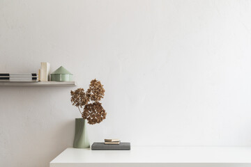 Desk with dried plant, office supplies, books and white wall background.