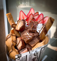 Close up bubble waffle with chocolate bars, ice cream and fresh strawberries, covered with chocolate topping