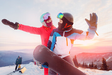 Happy lovers couple man and young women snowboarders on background of ski resort sunset. Concept...