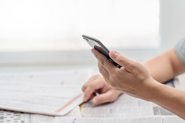 Close up hand a man holding smartphone looking news from the internet and many newspapers on the table in the background