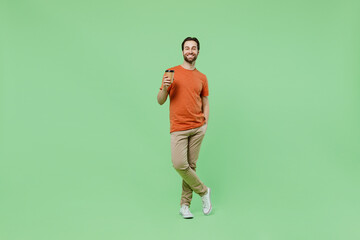 Fototapeta na wymiar Full body young man 20s wear orange t-shirt hold takeaway delivery craft paper brown cup coffee to go isolated on plain pastel light green color background studio portrait. People lifestyle concept.