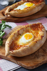 Khachapuri in Adjarian, Open pie with suluguni cheese and egg yolk in the form of a boat on wooden board, Traditional Georgian cuisine