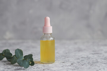 Bottle of cosmetic essential oil with dropper and eucalyptus leaf close-up. Serum skin care products with vitamin C. Beauty concept