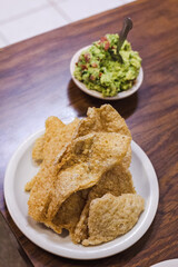 Crunchy mexican chicharron.  Several pieces of pork rinds served on a beige plate and guacamole bowl on wooden background. Mexican traditional food, snack concept.