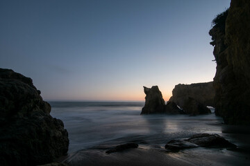 A pink sunsets against ocean rocks, Malibu California