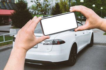 Smartphone mockup in the hands of a man. Against the background of a white electric car.
