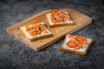Home made bread on a wooden cutting board with curd cheese, salmon and herbs