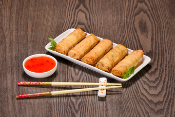 A delicious plate of egg rolls with a side of dipping sauce.