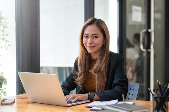 Portrait Of Smiling Young Beautiful Asian Businesswoman Sitting With Laptop Computer Looking At Camera In The Office.