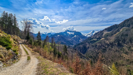 Fototapeta na wymiar Scenic view of a hiking trail leading to the snow capped mountain peaks of Karawanks near Sinacher Gupf in Carinthia, Austria. Mount Wertatscha and Hochstuhl (Stol) is visible in early spring.Rosental