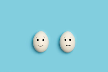 Huevos blancos con cara sonriente y feliz sobre un fondo celeste liso y aislado. Vista superior....