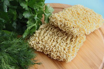 instant pasta on a wooden stand and fresh parsley and dill on a blue background