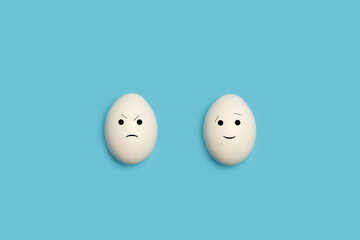 Huevos blancos con  gesto sonriente feliz y enfado triste sobre un fondo celeste liso y aislado....