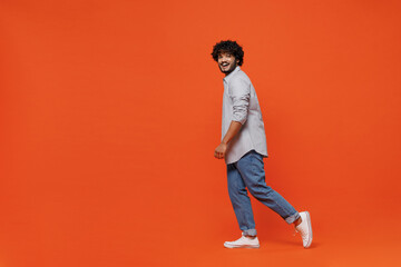 Fototapeta na wymiar Full size body length side profile view blithesome excited jubilant charismatic young bearded Indian man 20s years old wear blue shirt pace walking isolated on plain orange background studio portrait