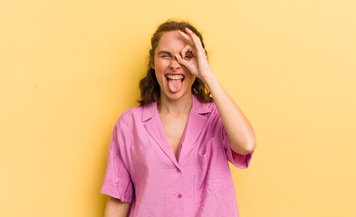 young pretty woman smiling happily with funny face, joking and looking through peephole, spying on...