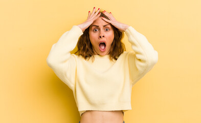 young pretty woman feeling horrified and shocked, raising hands to head and panicking at a mistake