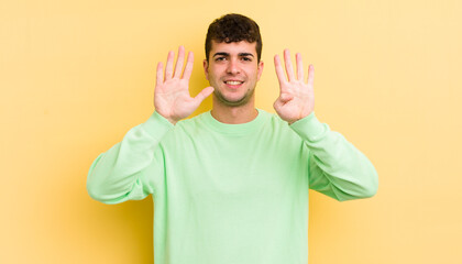 young handsome man smiling and looking friendly, showing number nine or ninth with hand forward,...