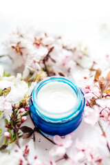 Obraz na płótnie Canvas Hygienic skincare lotion product. Herbal spa cosmetic cream with pink cherry flowers in a blue glass jar.