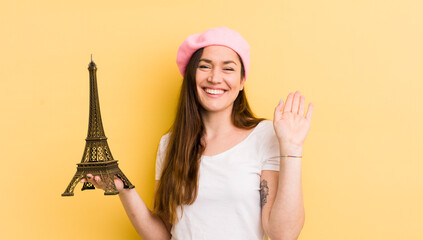 young pretty woman smiling happily, waving hand, welcoming and greeting you. paris concept © kues1