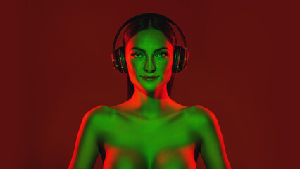 Beautiful woman listens music in headphones around colourful neon
