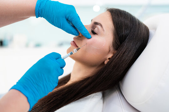 Beautician is contouring the woman's cheekbones with hyaluronic acid filler. Hyaluronic acid filler is injected by needle or cannula. Face contouring concept.