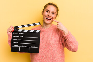 young pretty woman smiling confidently pointing to own broad smile. cinema clapper concept