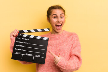 young pretty woman looking excited and surprised pointing to the side. cinema clapper concept