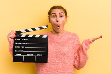 young pretty woman looking surprised and shocked, with jaw dropped holding an object. cinema...