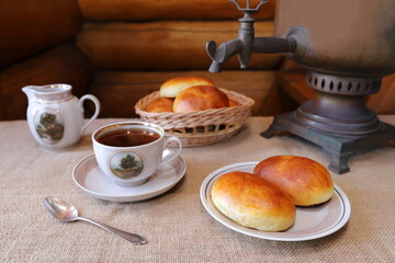 Homemade pies on a plate near an old ceramic utensil against the background of vintage samovar. 