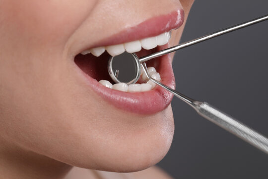 Examining woman's teeth with dentist's mirror on grey background, closeup