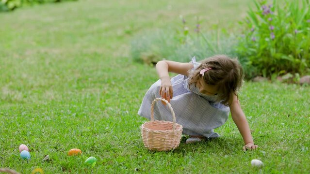 Girl find and pick up multicolored egg on Easter egg hunt in garden