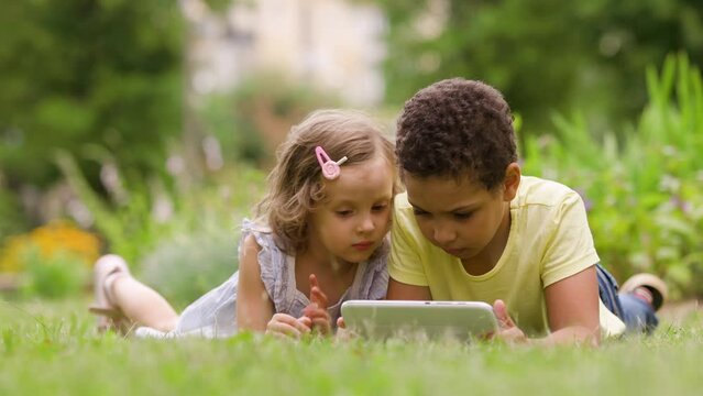 Children is lying on the lawn with a tablet in his hands. The child uses the gadget in nature. mobile devices are everywhere